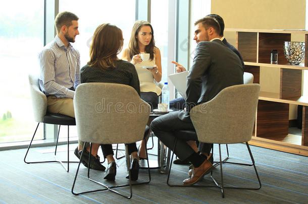 一群五个年轻人在一<strong>起坐</strong>在办公室的桌子上讨论一些事情