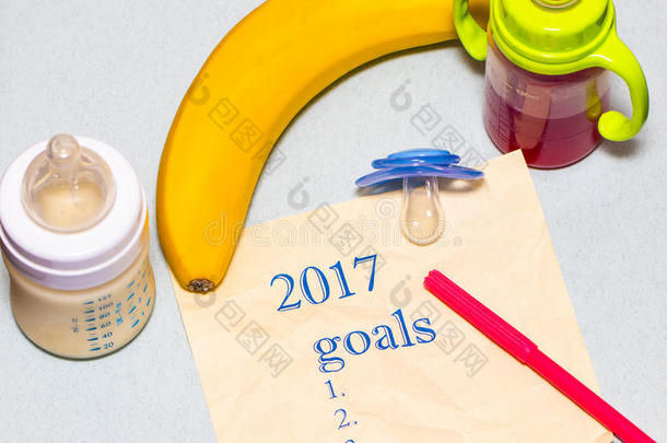 在一张纸上列出2017年的目标清单，上面有一个奶嘴和一个蓝色背景的婴儿瓶