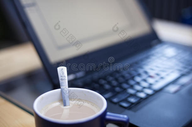 一杯咖啡，<strong>上面</strong>印有咖啡标志的茶匙，背景中有一台<strong>笔记本</strong>电脑