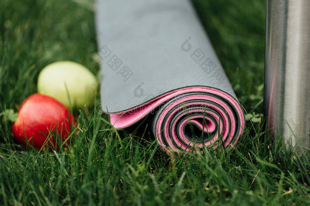 在草<strong>地上</strong>的公园里，有吸引人的灰色粉红色<strong>滚动</strong>瑜伽或健身垫，里面有苹果和热水瓶。