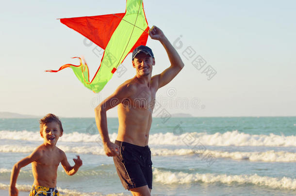 父亲带着儿子，日落在海边玩风筝，幸福的家庭