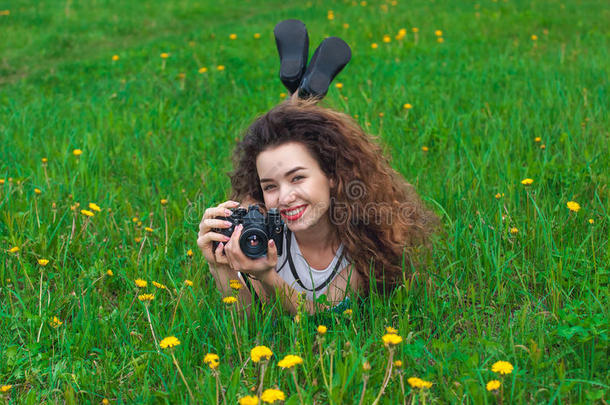 美丽，有吸引力的女孩<strong>摄影</strong>师，卷发，拿着相机，躺在草地上盛开的<strong>蒲公英</strong>