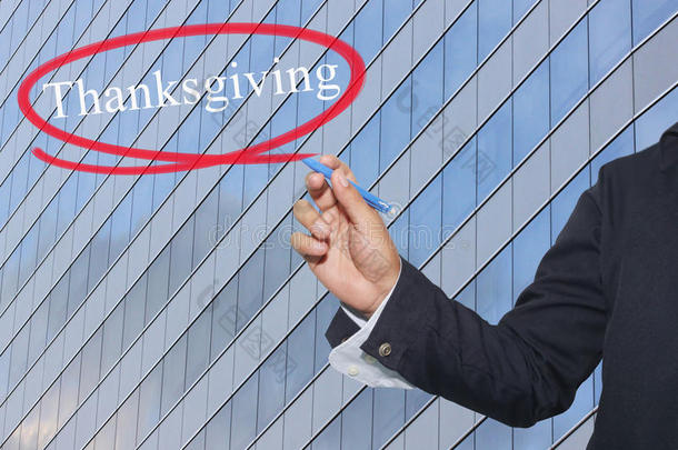 年轻商人的手在摩天大楼的背景上写着感恩节这个词。
