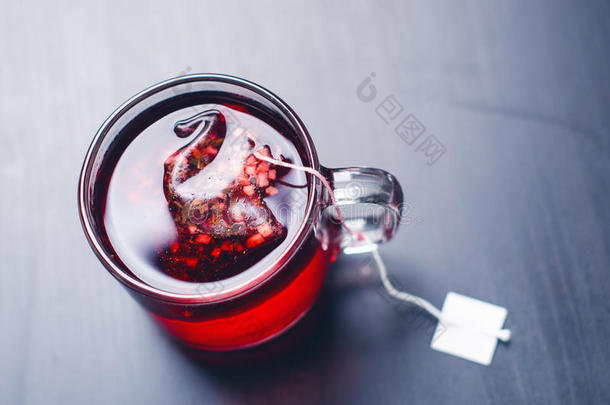 一杯带茶桶的热茶。 在一个自然的，黑暗的背景上。 杯子来自透明的玻璃