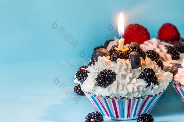 蛋糕上有奶油和浆果，蓝色背景上有<strong>一支</strong>点燃的蜡烛