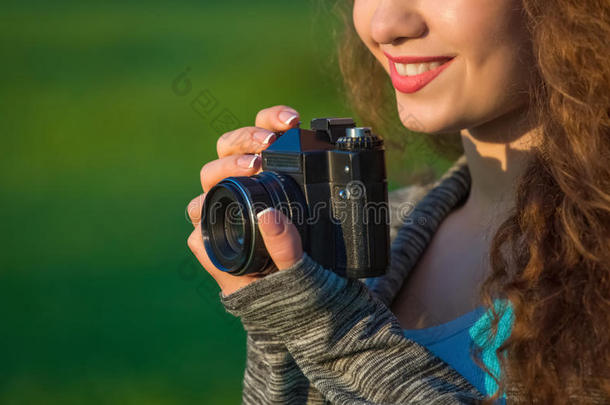 美丽的女孩-摄影师，卷发，拿着一台旧相机，在春天的户外公园里拍照。