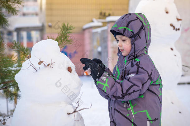 有趣的小男孩<strong>堆雪人</strong>，吃胡萝卜，玩雪，在寒冷的一天<strong>户外</strong>玩。 积极的休闲儿童