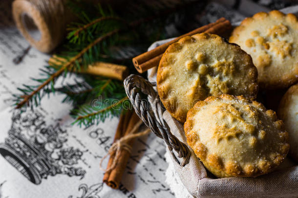 圣诞馅饼在柳条篮子里，放在老式布上，上面有肉桂棒和冷杉树枝