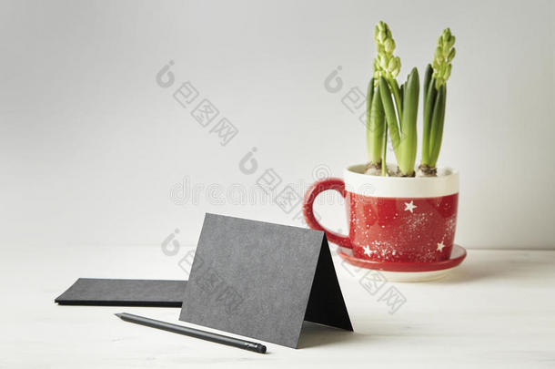 白色木桌上的黑色纸卡或明信片，<strong>版面</strong>空间。 红色罐子里的花