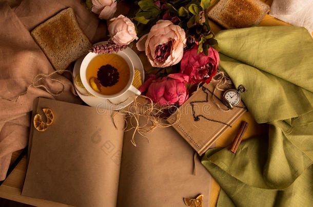 工艺纸笔记与一杯茶，花，牡丹，老古董时钟。 复古背景。 现代色调。 文本的合作空间，图片