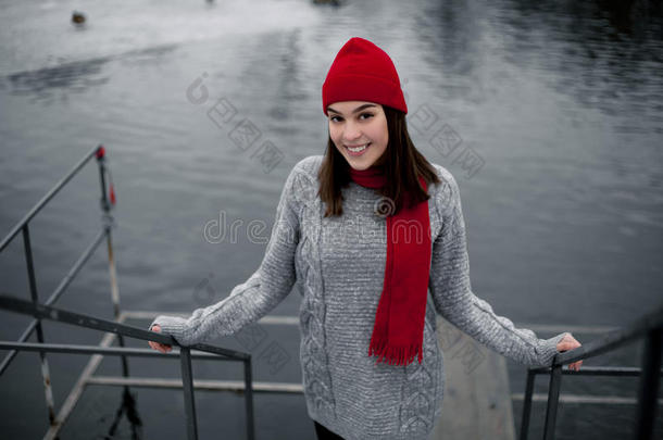戴着红色帽子和围巾的女孩在湖边的冬季公园散步。