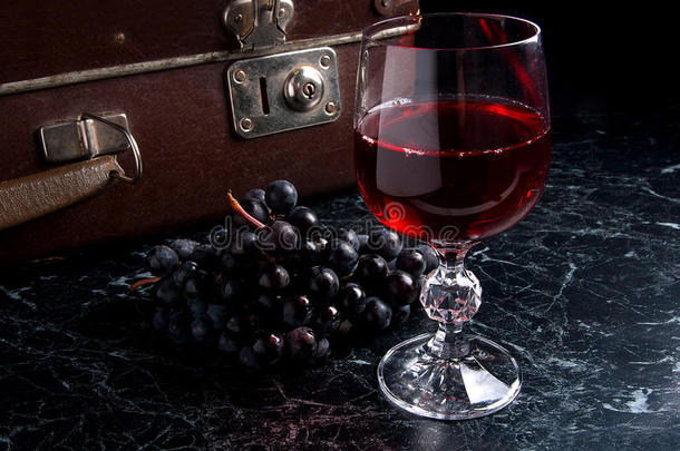 <strong>深色大理石</strong>背景上的一杯红酒。 背面背景上的一簇蓝色葡萄。