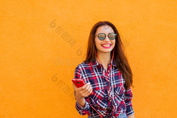 漂亮时尚的女人带着智能手机和耳机。 飞毛。 橙色背景。 复制空间