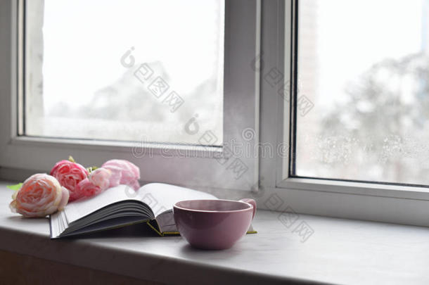 舒适的家庭静物：一杯热咖啡，春天的鲜花，打开的书与温暖的格子在窗台上抵御雪