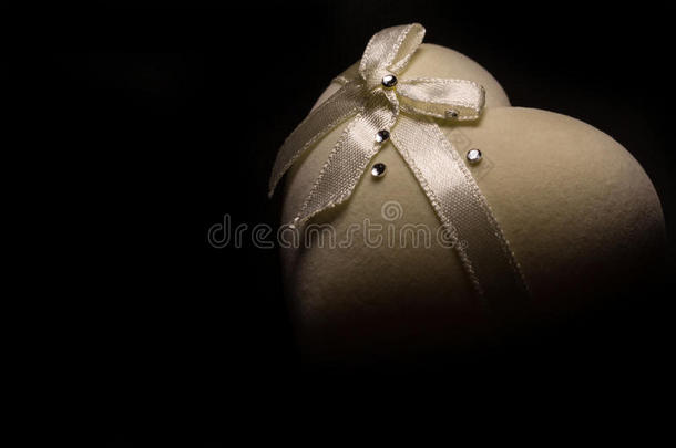 美丽的柔软的心形盒子米色，顶部有蝴蝶结，黑色背景