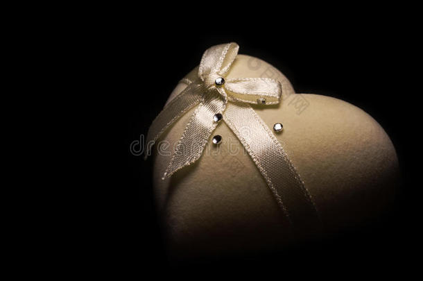 美丽的柔软的心形盒子米色，顶部有蝴蝶结，黑色背景