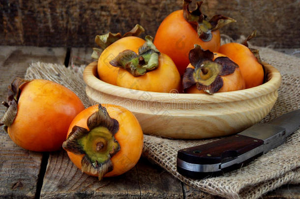 美味的成熟橙色柿子在碗中的木制背景。