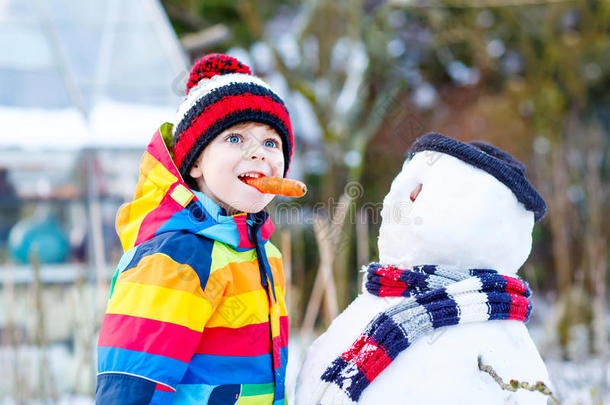 有趣的男孩穿着五颜六色的衣服在户外堆雪人