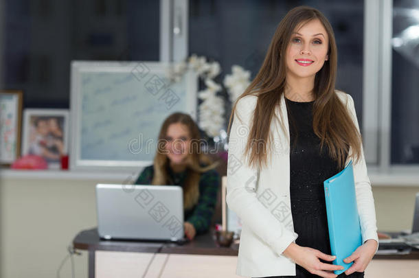 美丽微笑的女商人在办公室里拿着文件，女人在后台工作。