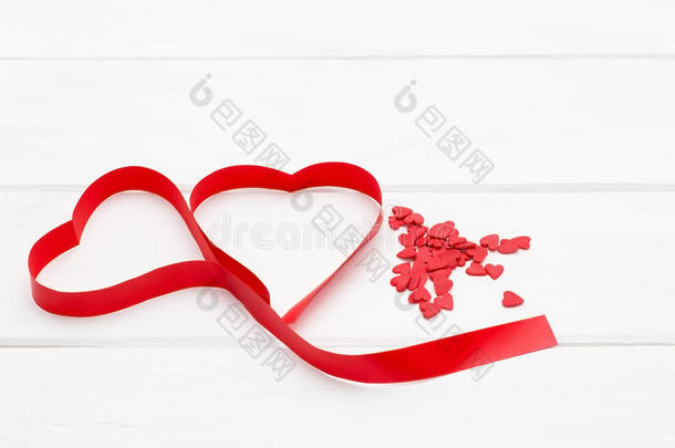 许多小红心和一条红色丝带的心的形式在白色的木制背景上。