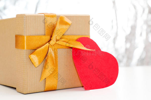 金色丝带和红色心的礼品盒躺在<strong>银光</strong>闪闪的背景上的白色桌子上。