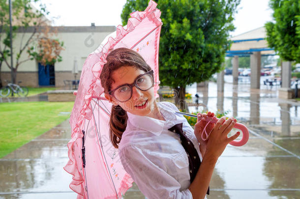 戴着领带和大眼镜的女孩站在粉红色的雨伞下