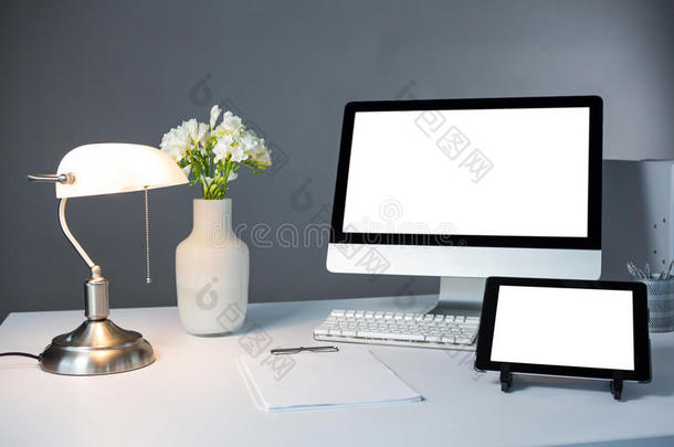 台式电脑，数码平板电脑和台灯，桌上有花瓶