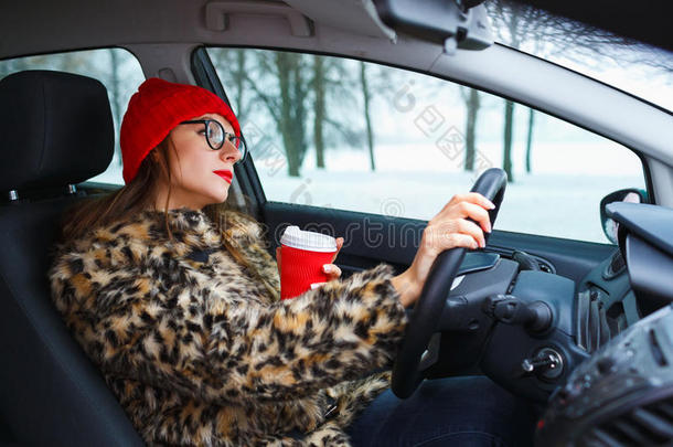 穿着毛皮大衣和红色帽子的美女带着咖啡开车去