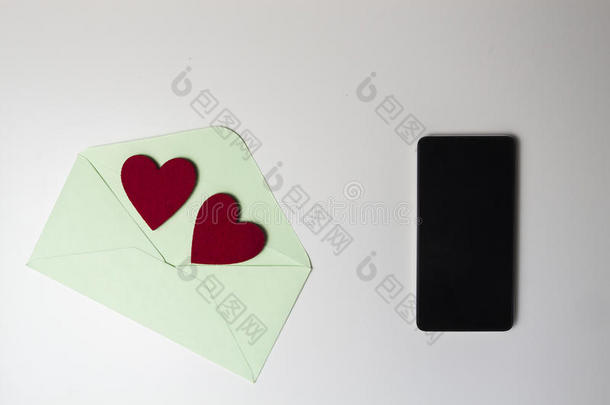 绿色信封，白色桌子上有两颗红心和手机。 上面的风景。