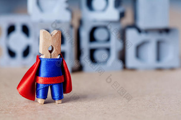 可爱的玩具超级英雄角色。 穿蓝色西装和红色斗篷的衣夹。 灰色积木背景
