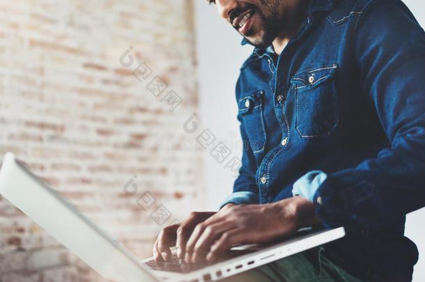 留着胡子的非洲年轻人微笑着使用笔记本电脑，坐在他的现代同事的地方。快乐商业的概念