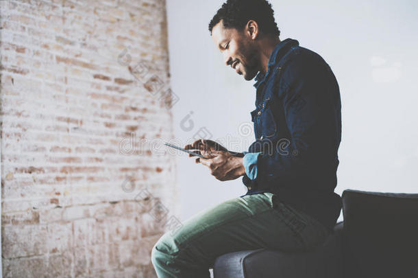有魅力的留着胡子的非洲人，坐在他现代家庭办公室的沙发上使用平板电脑。年轻人的概念
