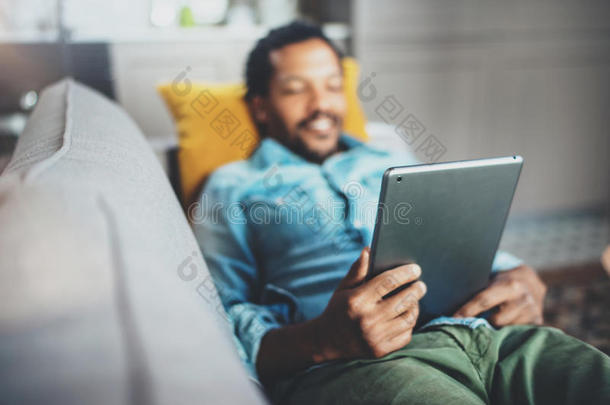 迷人的留胡子非洲年轻男士沙发和现代平板电脑家庭概念喜欢移动的人