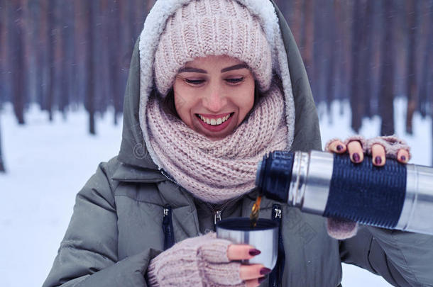 女人在雪林里把茶从<strong>热水</strong>瓶倒到<strong>杯子</strong>里