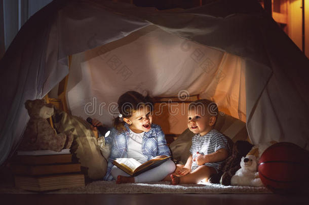 孩子们男孩和女孩在帐篷里用手电筒看书