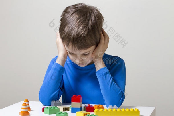 集中的孩子坐着，俯视着桌子上五颜六色的塑料建筑玩具块
