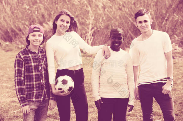 女孩和三个男孩在春天的公园踢足球，微笑着
