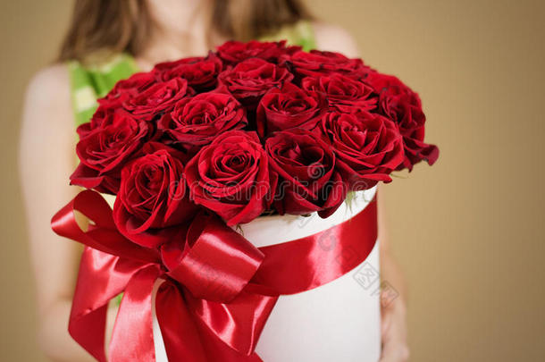 女孩手里拿着丰富的礼物花束，21朵红玫瑰。 白色帽子盒中花朵的组成。 用宽的红色丝带和b绑在一起