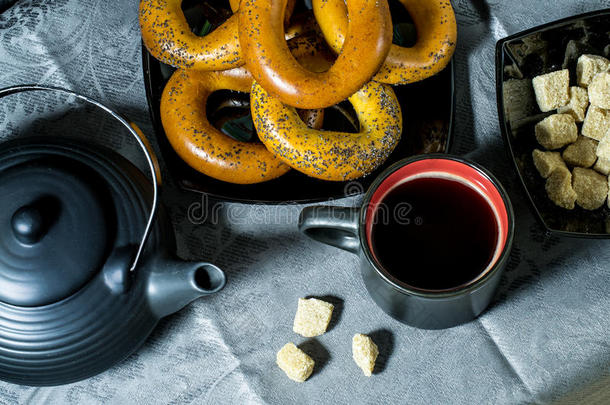 百吉饼，咖啡杯，茶壶和黑色的糖在蓝色桌布上。 从上面看