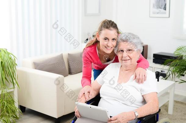 开朗的年轻女孩用电脑平板电脑教互联网，和一位坐在<strong>轮椅</strong>上的<strong>老年</strong>妇女分享时间