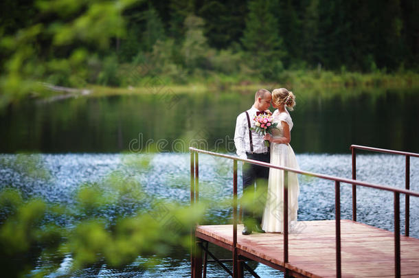 美丽的年轻新婚夫妇，新娘和新郎在湖底摆姿势。 新郎和新娘在码头。