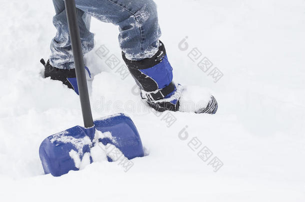 穿着靴子和牛仔裤的男人的下半身，拿着铲子站在雪地里。