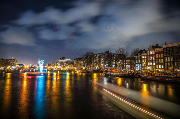 游船在夜间运河里奔腾。 在光明节内阿姆斯特丹夜间运河上的灯光装置。