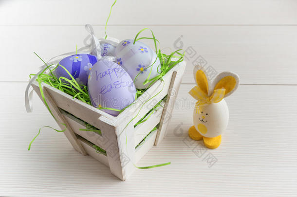 复活节小篮子，有彩色鸡蛋和一个小鸡蛋兔子在木板上。