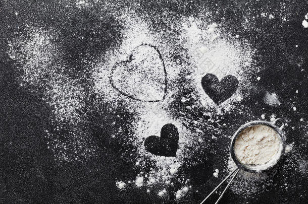 烘焙背景与面粉和心形厨房黑色桌子从上面为情人节烹饪。 平躺式。