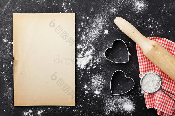 在<strong>厨房</strong>黑桌上用面粉、<strong>擀面杖</strong>、纸张和心形烘焙背景，用于情人节。