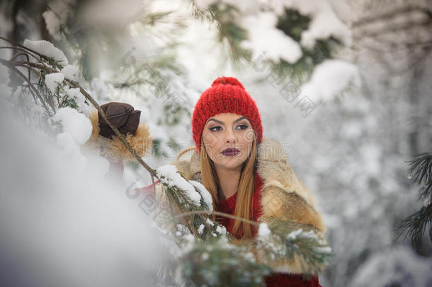 穿着红色棕色毛皮斗篷的美丽女人在森林里欣赏冬天的风景。 金发女孩在白雪覆盖的树枝<strong>下摆</strong>姿势
