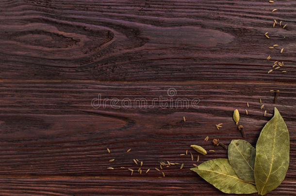 海湾树叶，丁香和香菜种子在木制的黑暗纹理背景