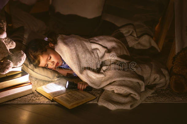 女孩睡在帐篷里，拿着书和手电筒