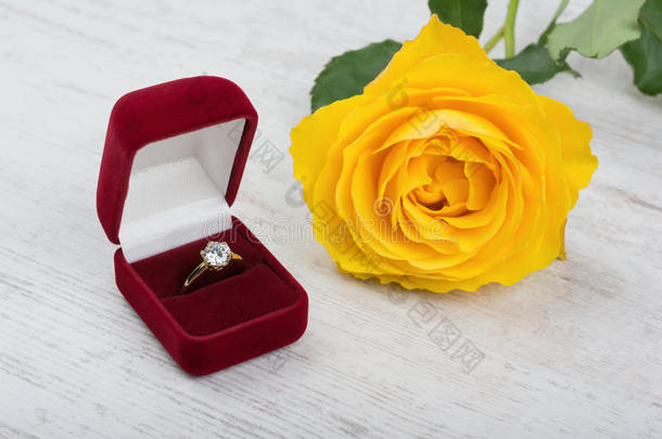 金色珍珠戒指在一个红色的礼品盒和黄色玫瑰在白色的木制背景